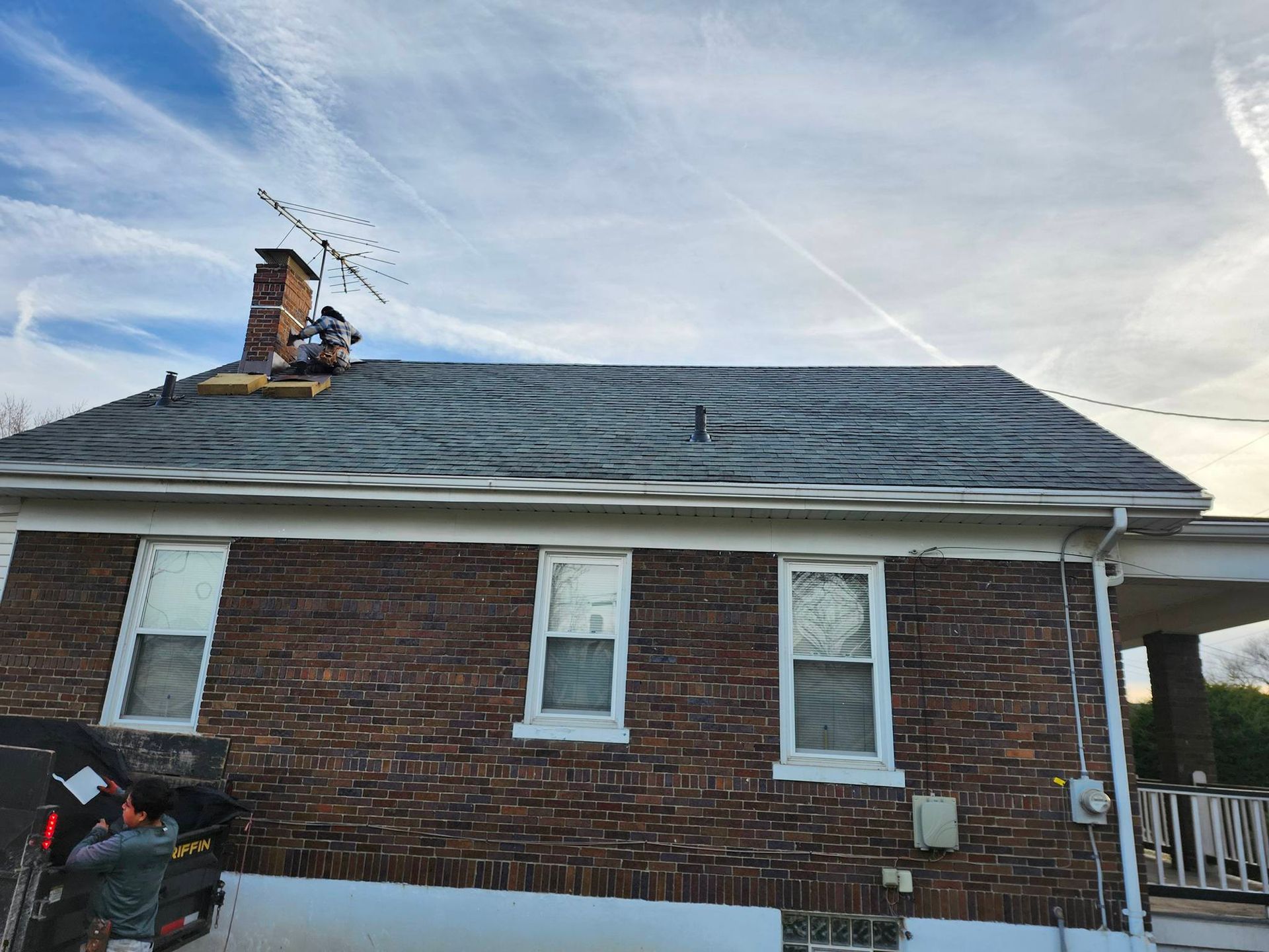 Brick house with a gray roof, chimney, and a black motorcycle parked beside it under a blue sky.
