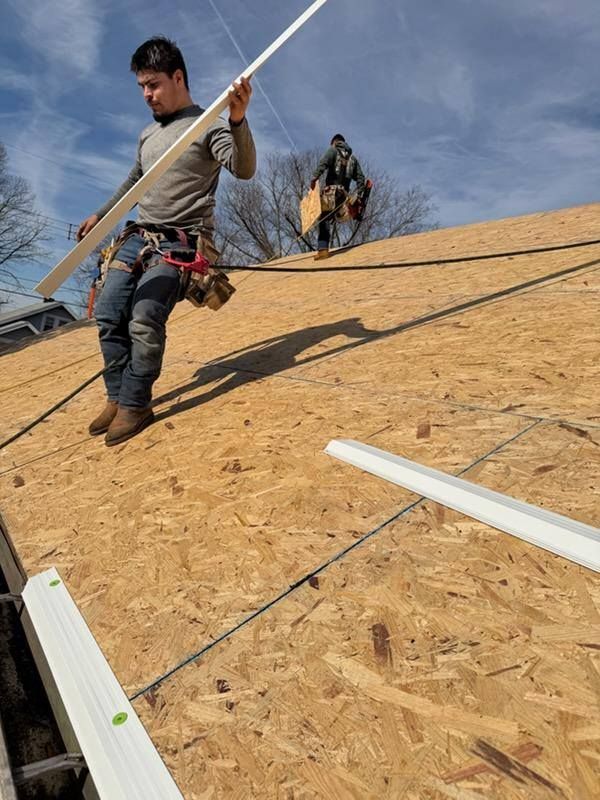 Roofers carrying materials up a steep OSB roof under construction.