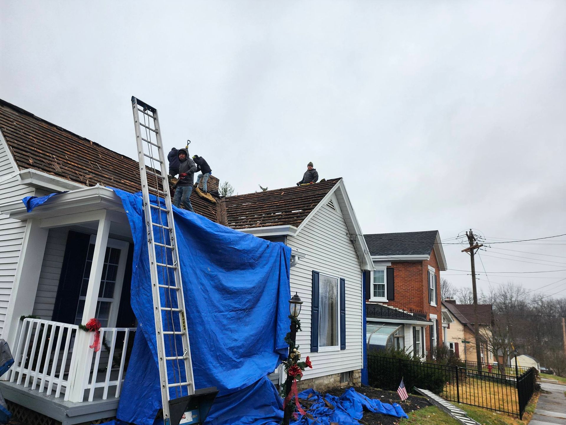 Workers on a house roof covered by a blue tarp during repairs after storm damage
