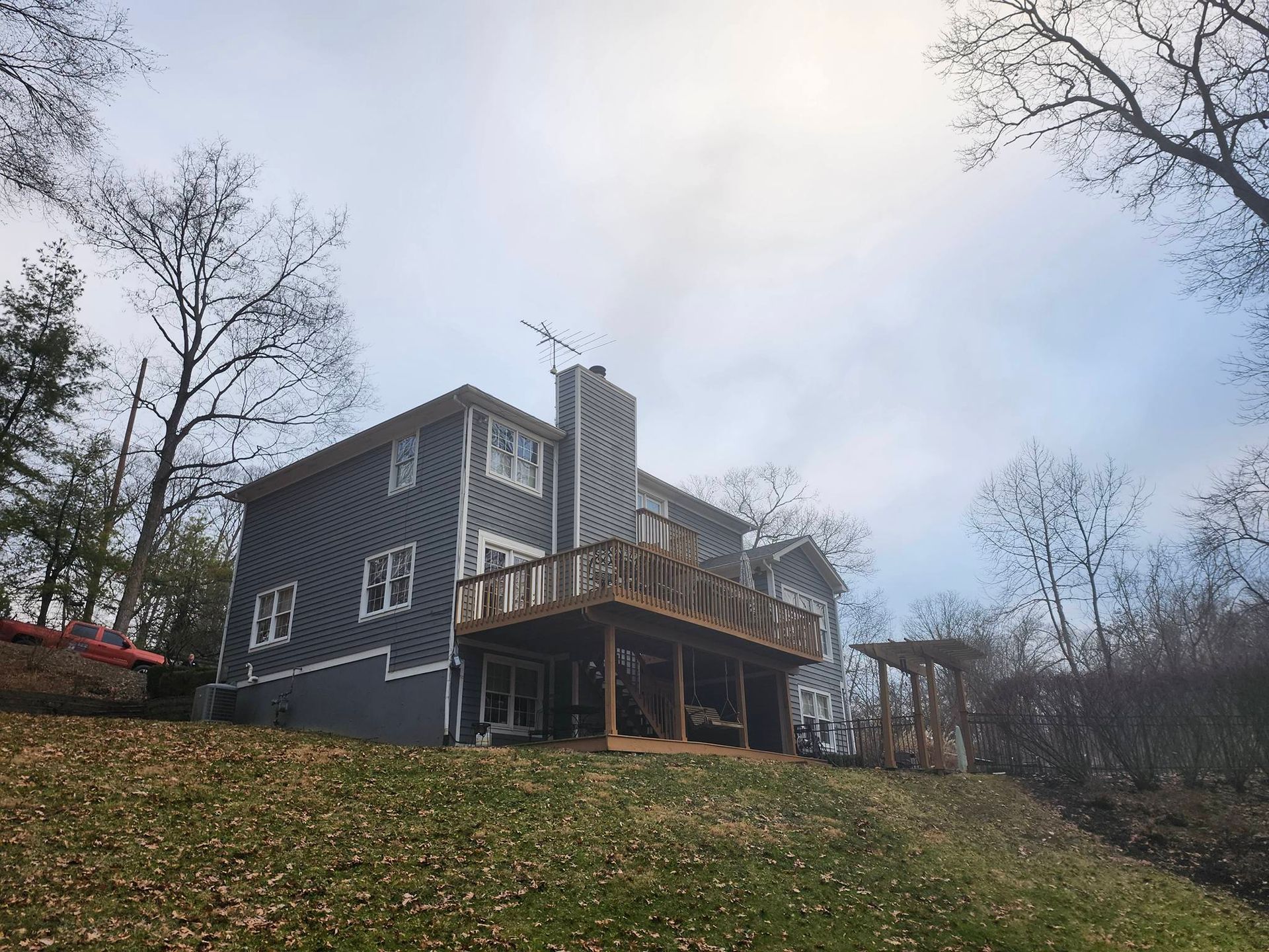 Gray house with a wooden deck on a grassy hillside under a cloudy sky