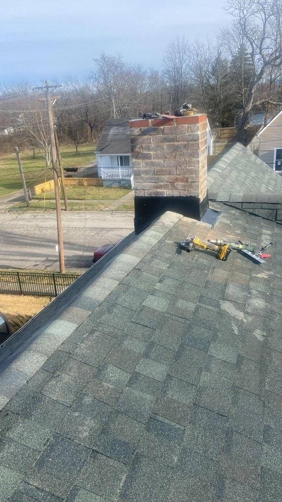 Roof with gray shingles and a brick chimney, with tools near the chimney on a sunny day.
