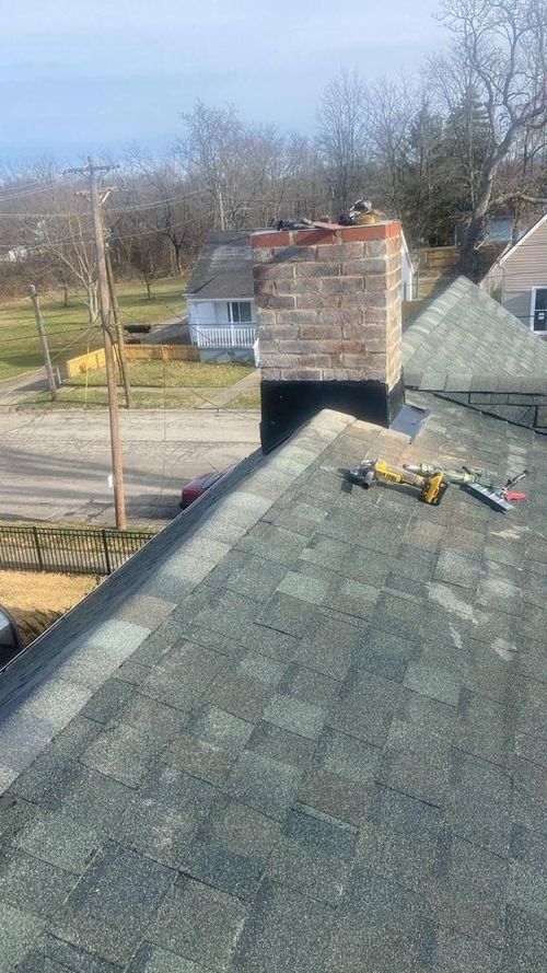 Roofer's ladder on a gray shingled roof beside a brick chimney on a sunny day