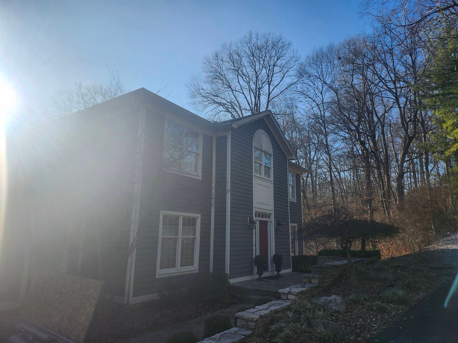 Two-story gray house with white trim beside trees on a sunny day