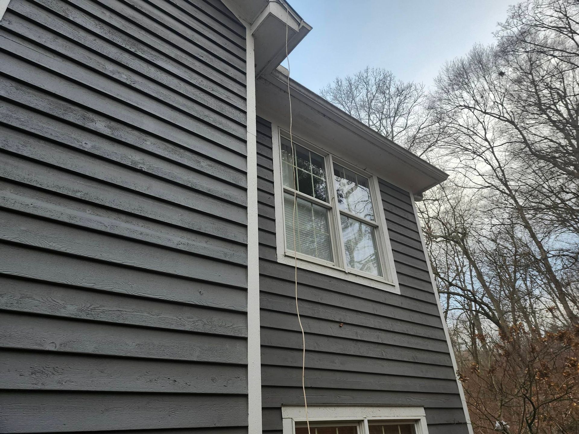 Gray house exterior with white trim and a window under bare trees