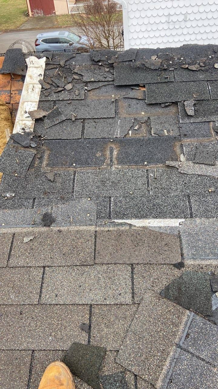 Damaged asphalt shingle roof with missing and curled shingles near the edge