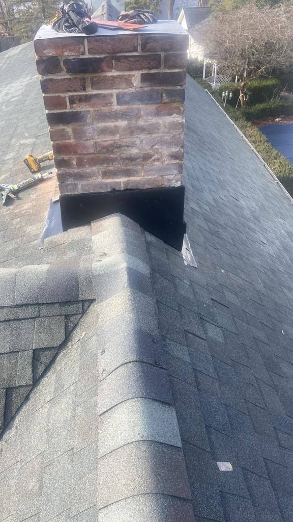 Brick chimney on a shingled rooftop, with a shadow cast across the roof peak.