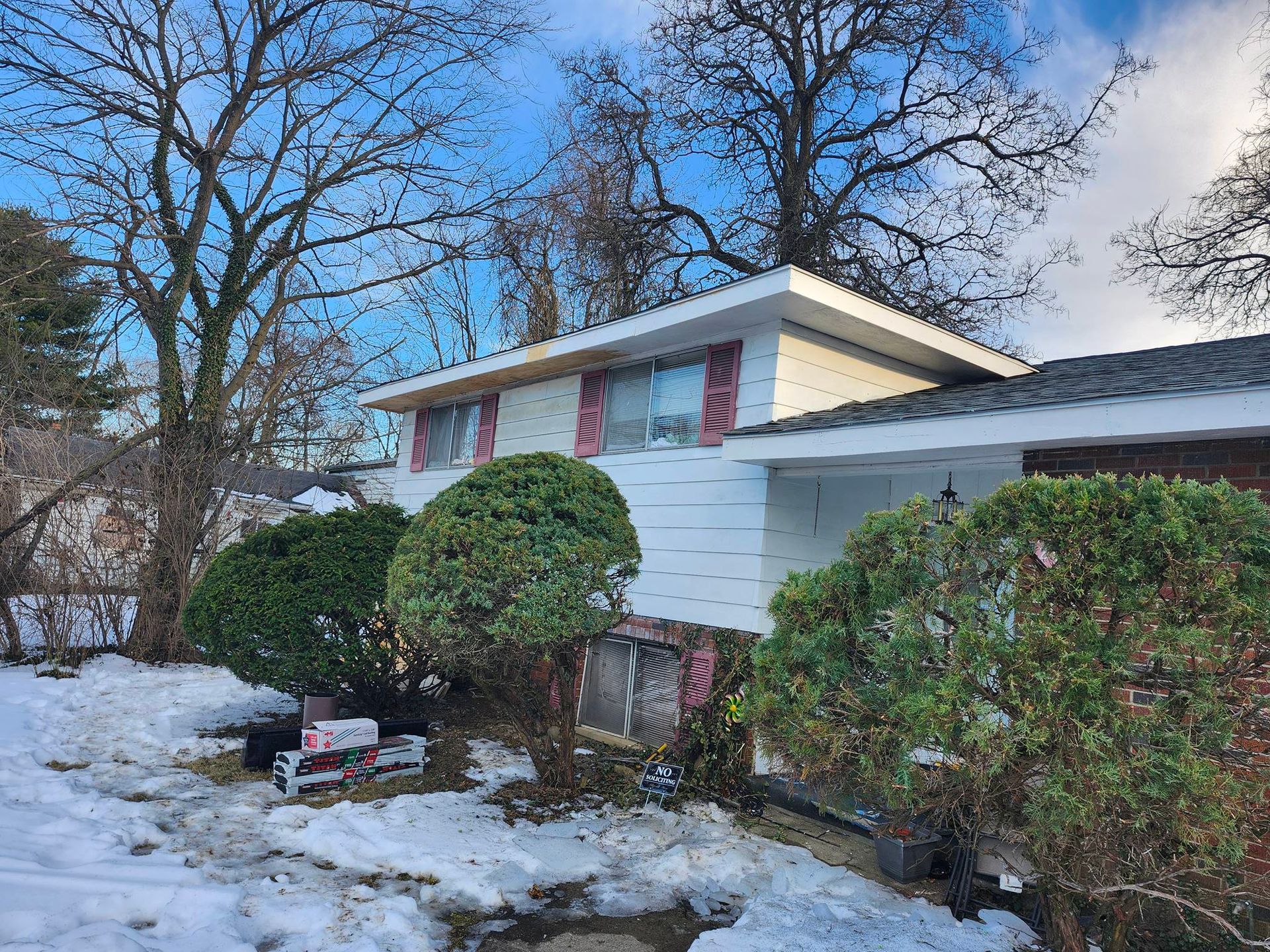Snowy house with trimmed shrubs and bare trees on a winter day
