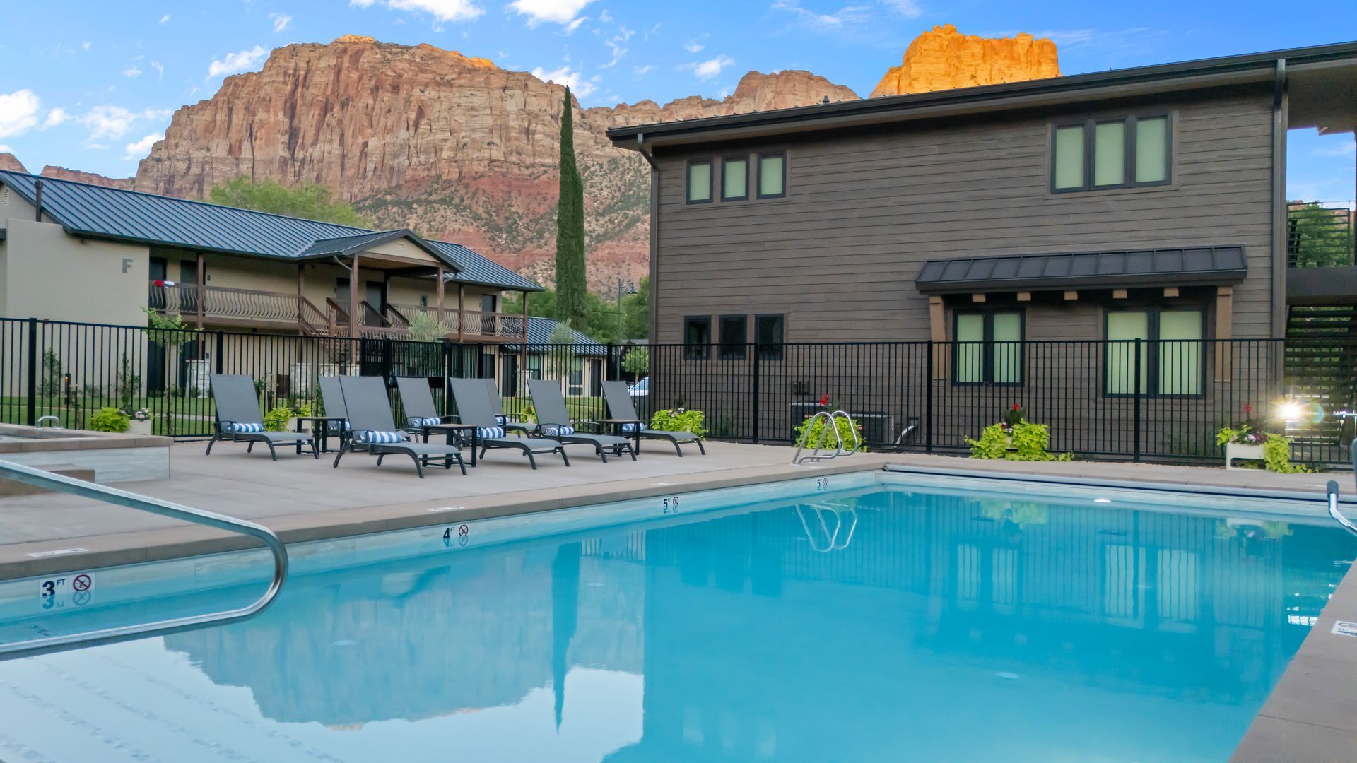 Swimming pool and lounge chairs at a resort, with brown buildings and a mountain backdrop.