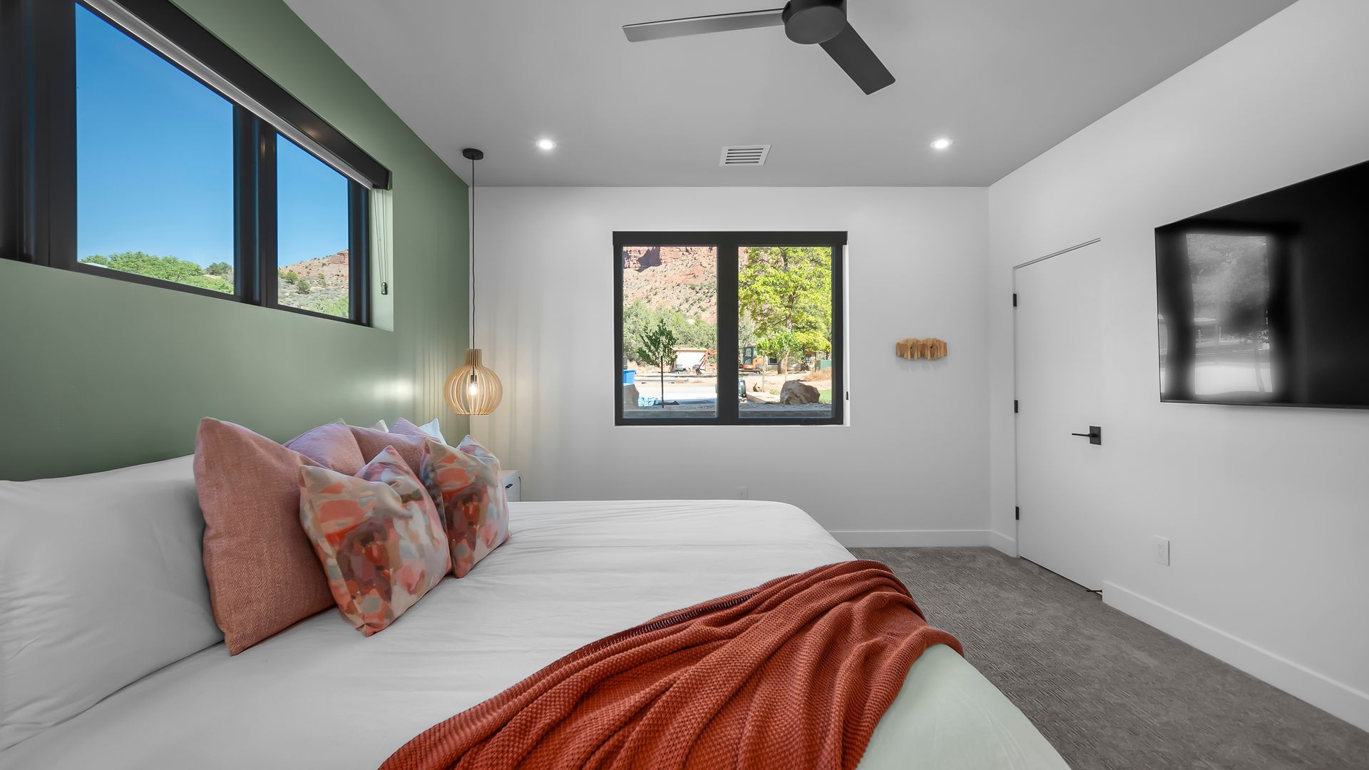 Bedroom with king bed, green wall, black-framed windows, TV, and ceiling fan.