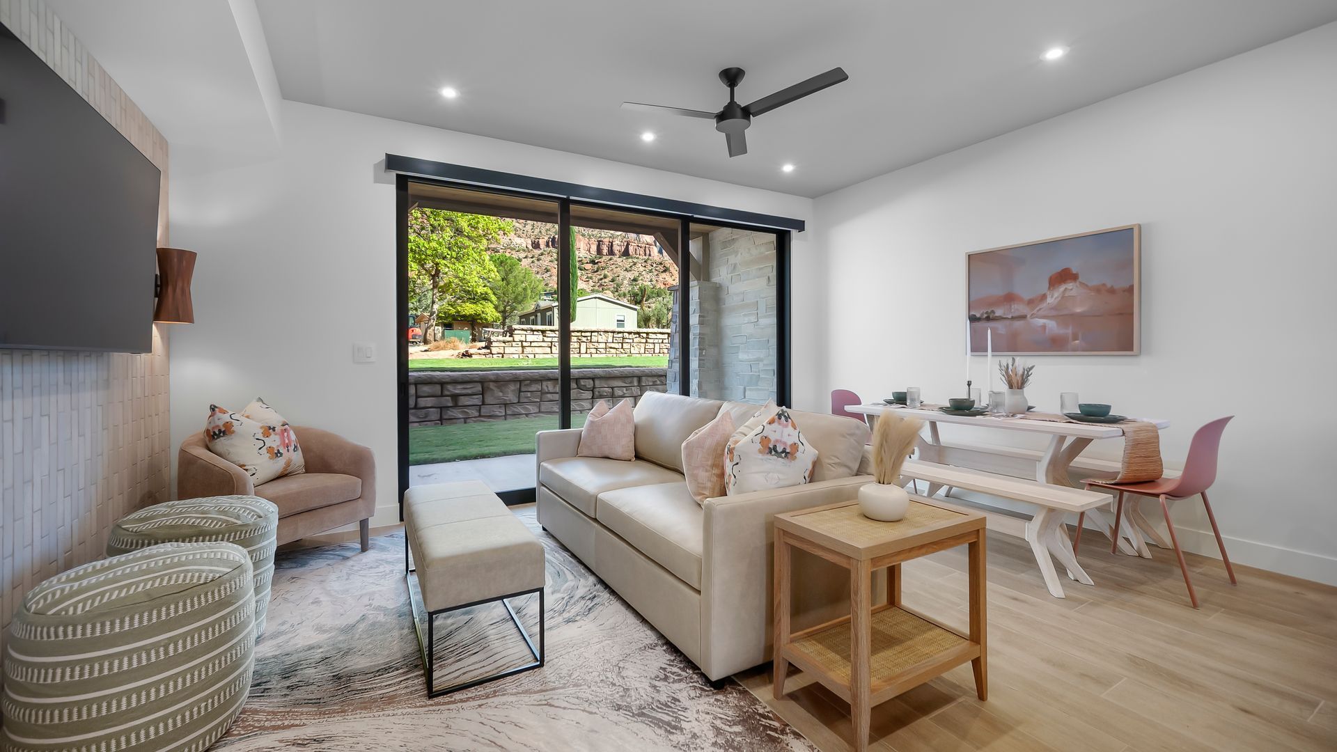 Living room with sofa, chairs, dining table, and large window overlooking a yard.