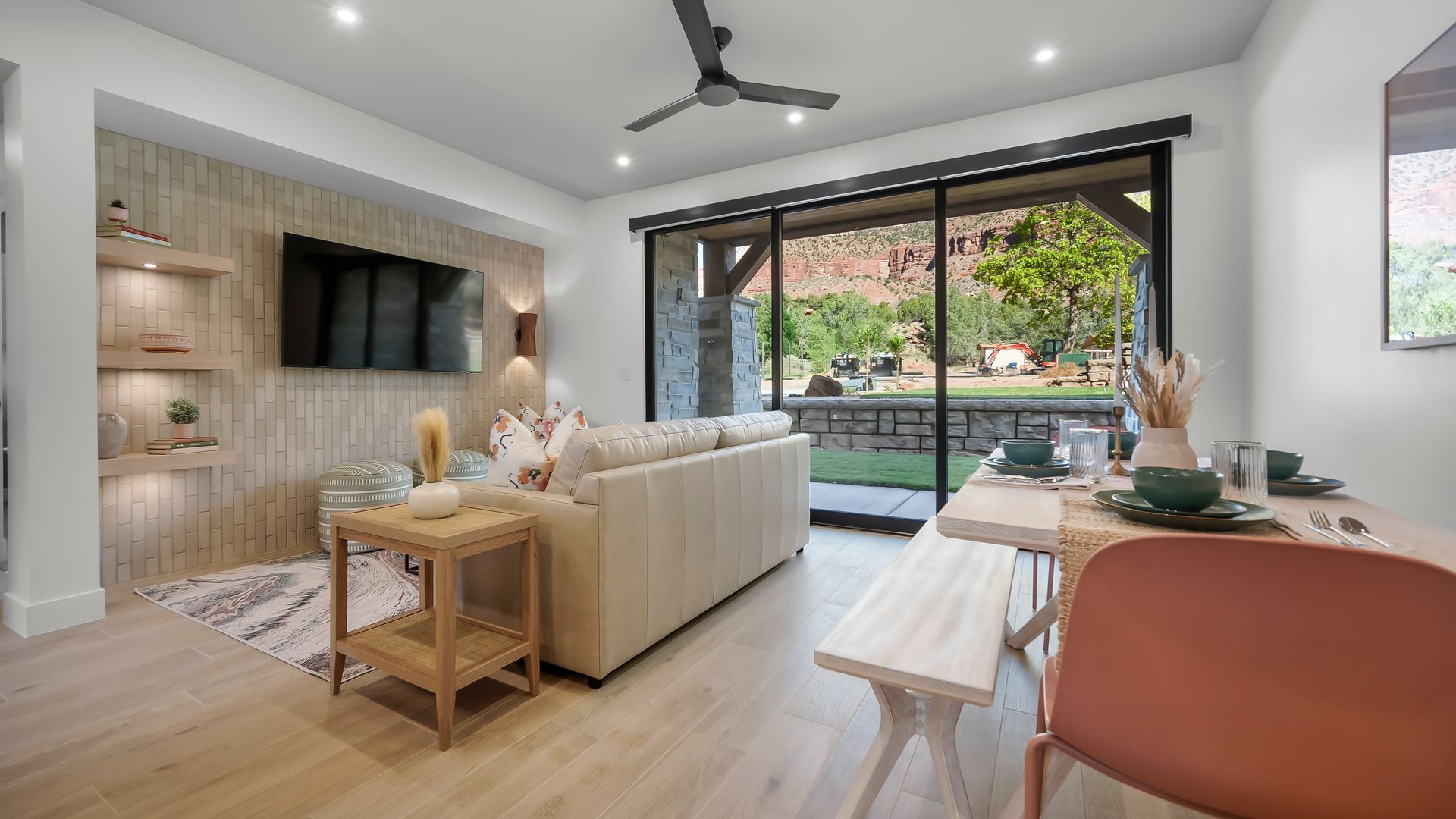 Living room with a sofa, TV, dining table, and large window overlooking a yard.