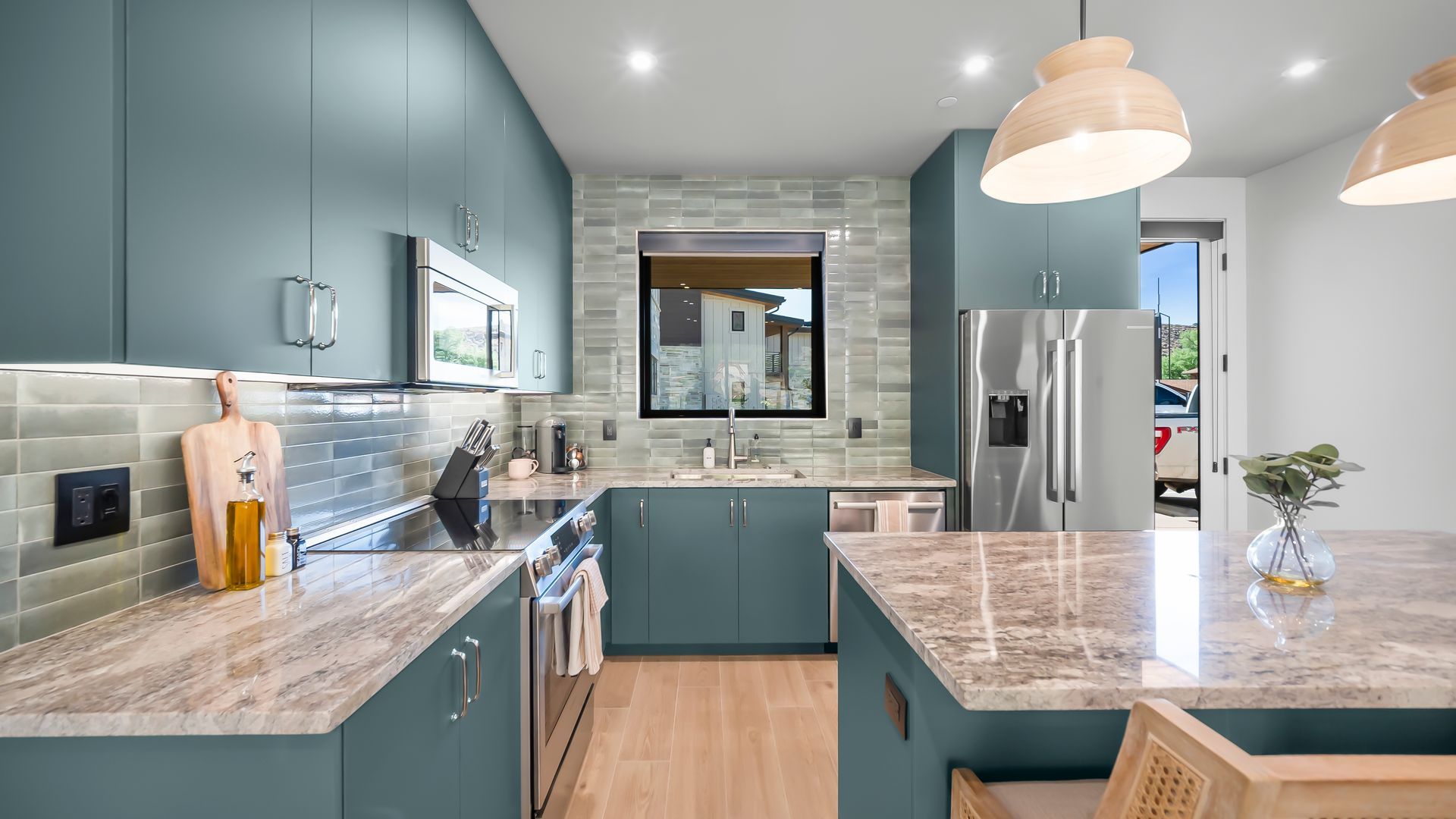 Modern teal kitchen with stainless steel appliances, light wood floors, and stone countertops.