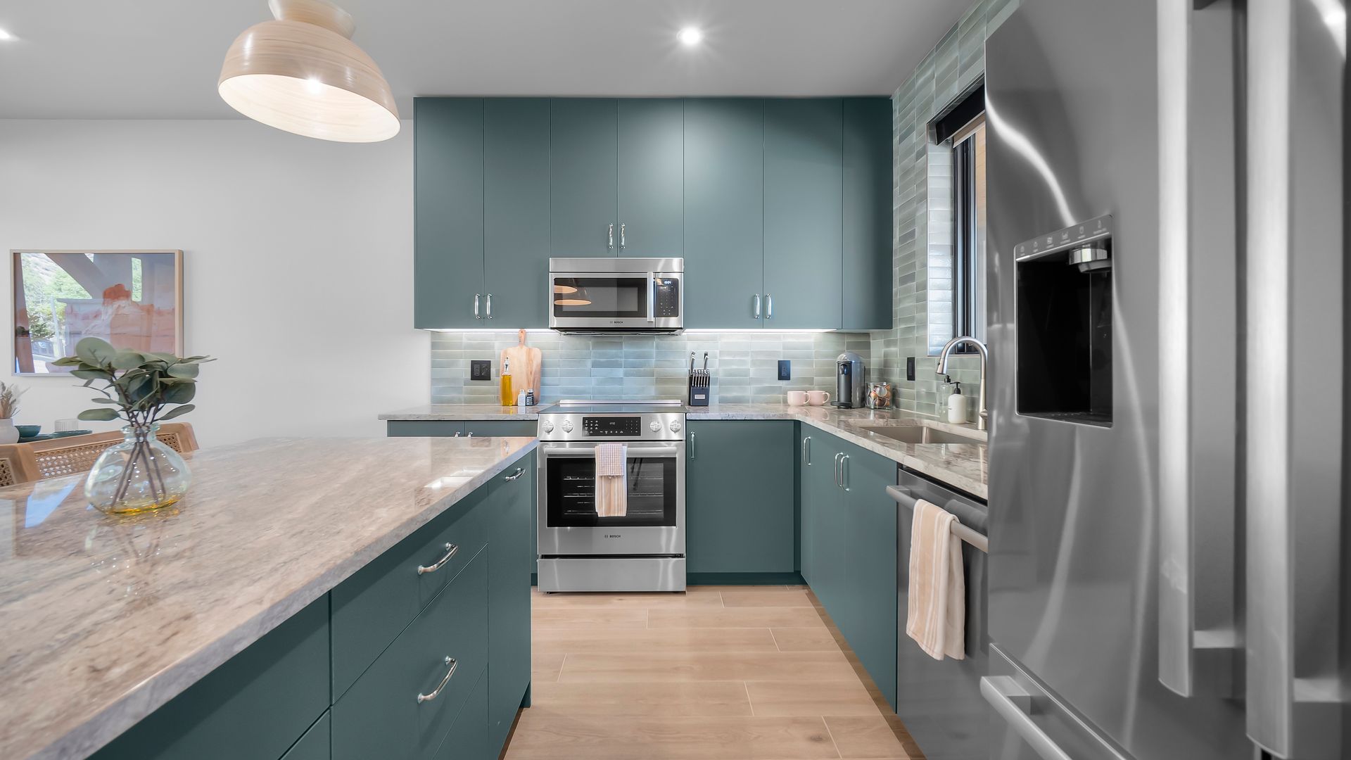 Modern kitchen with teal cabinets, stainless steel appliances, and a light-colored island.