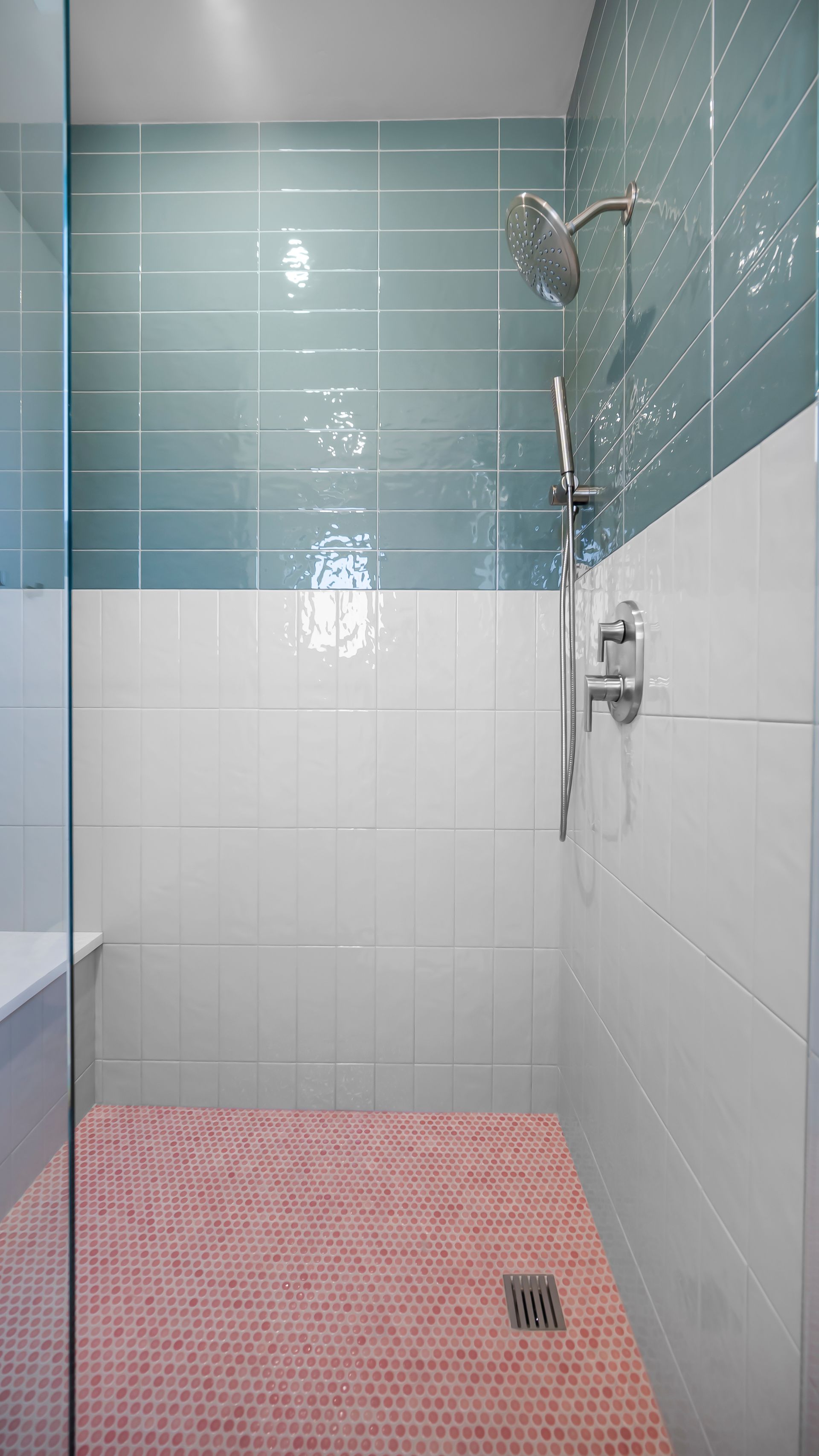 Shower with blue and white tile walls, pink tiled floor, glass door, and silver shower fixtures.