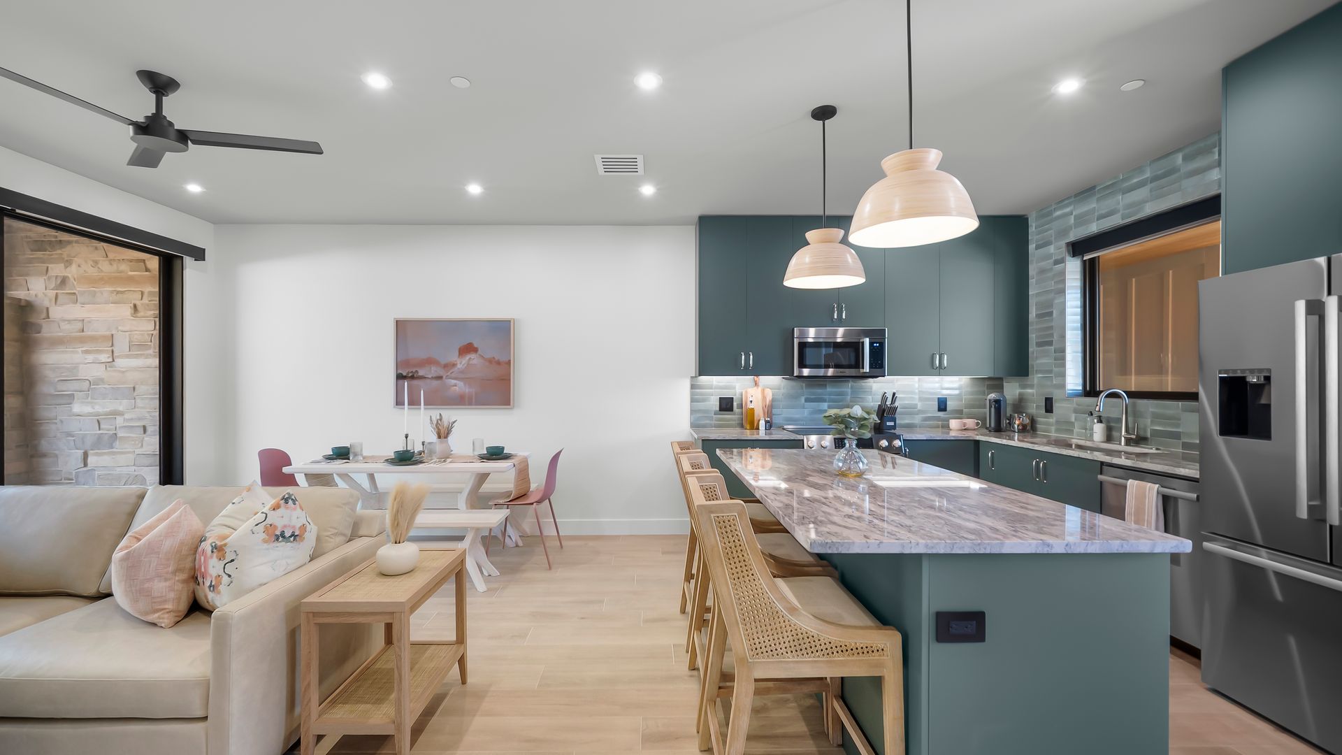 Modern kitchen and dining area with teal cabinets, light wood floors, and island with bar seating.