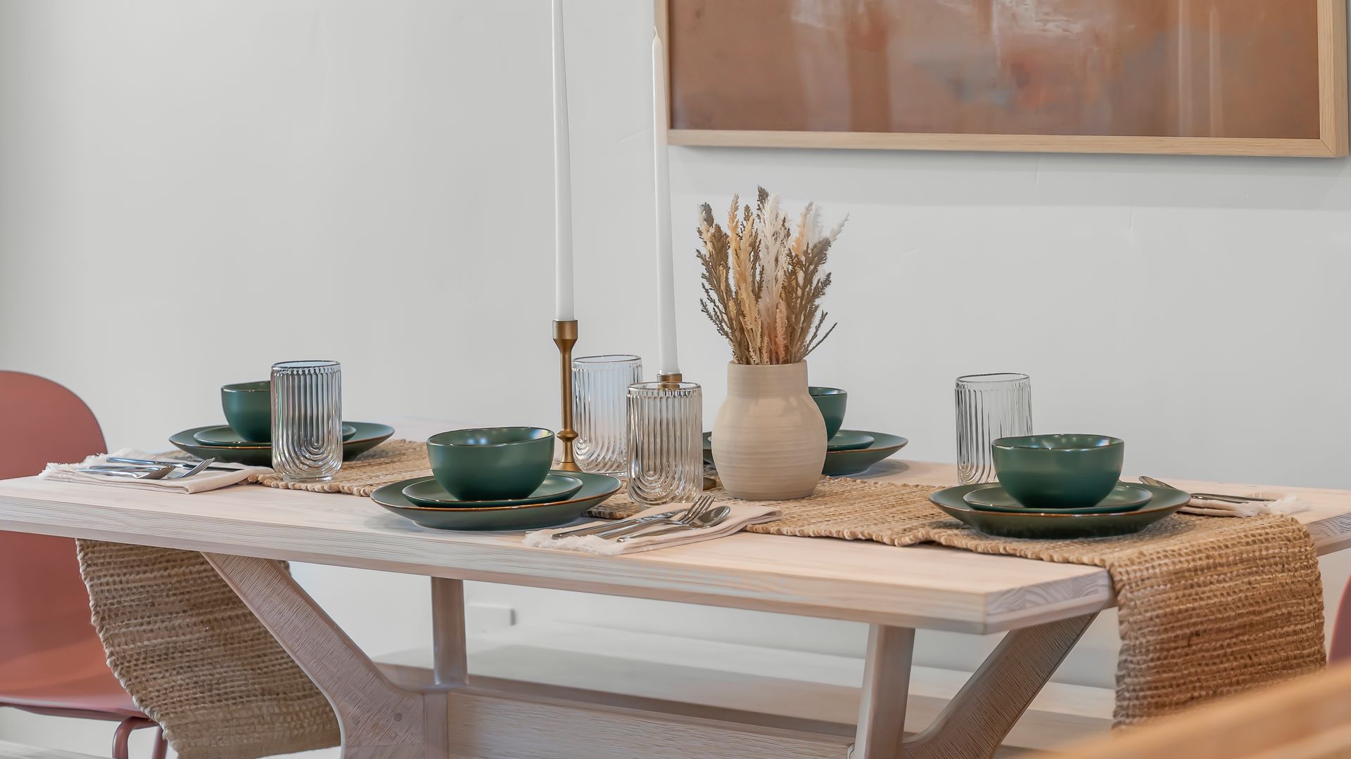 Dining table set with green tableware, candles, and a vase of dried flowers.