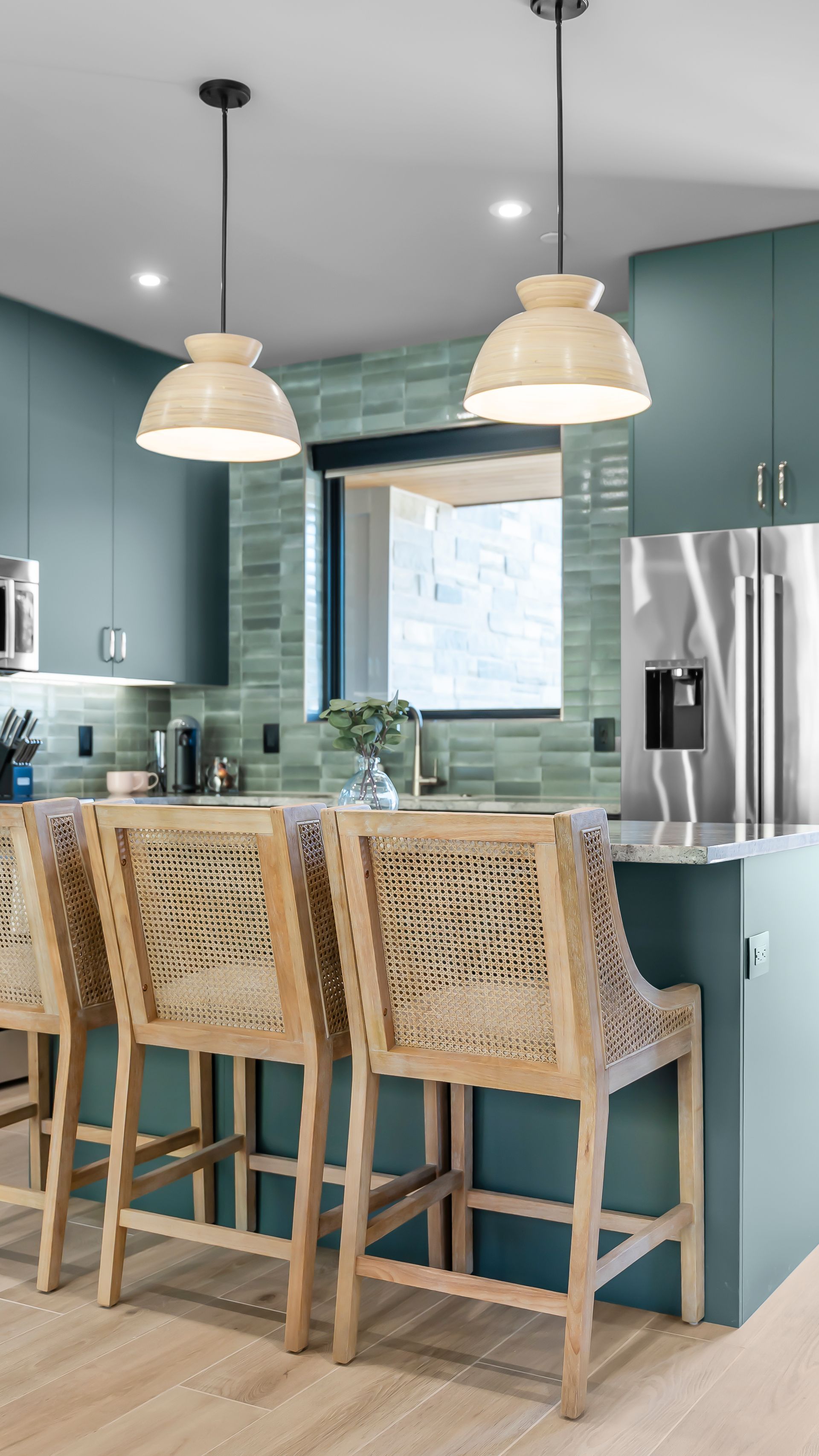 Kitchen with teal cabinets, woven barstools, pendant lights, and stainless steel refrigerator.