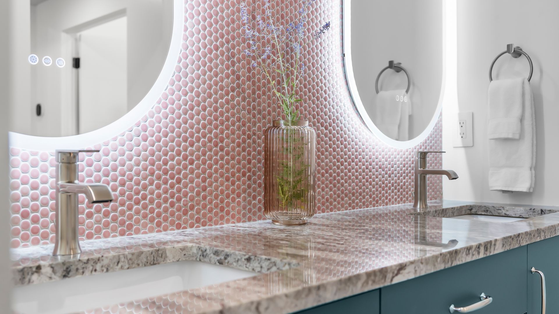 Modern bathroom with two round mirrors, copper mosaic tile, and teal vanity.