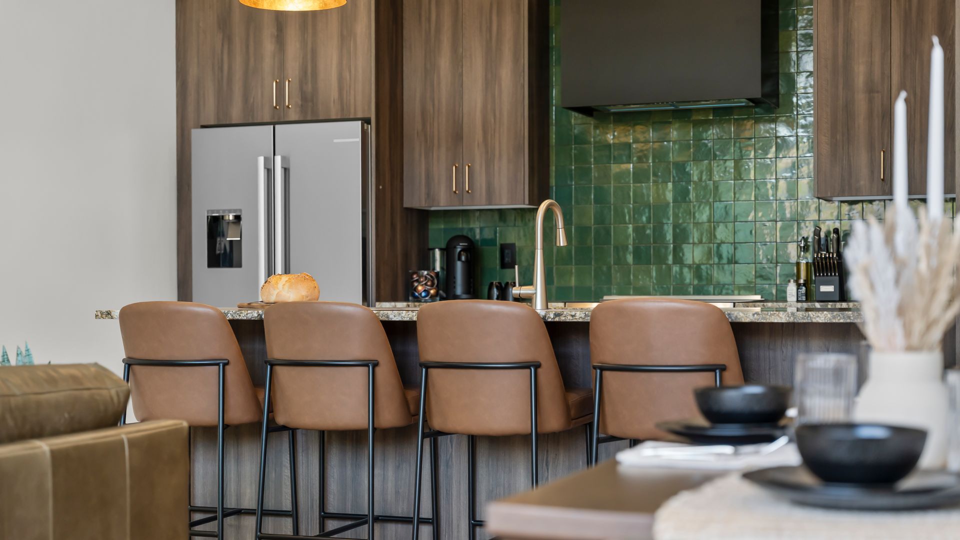 Modern kitchen with brown cabinetry, stainless steel fridge, and four brown leather bar stools.