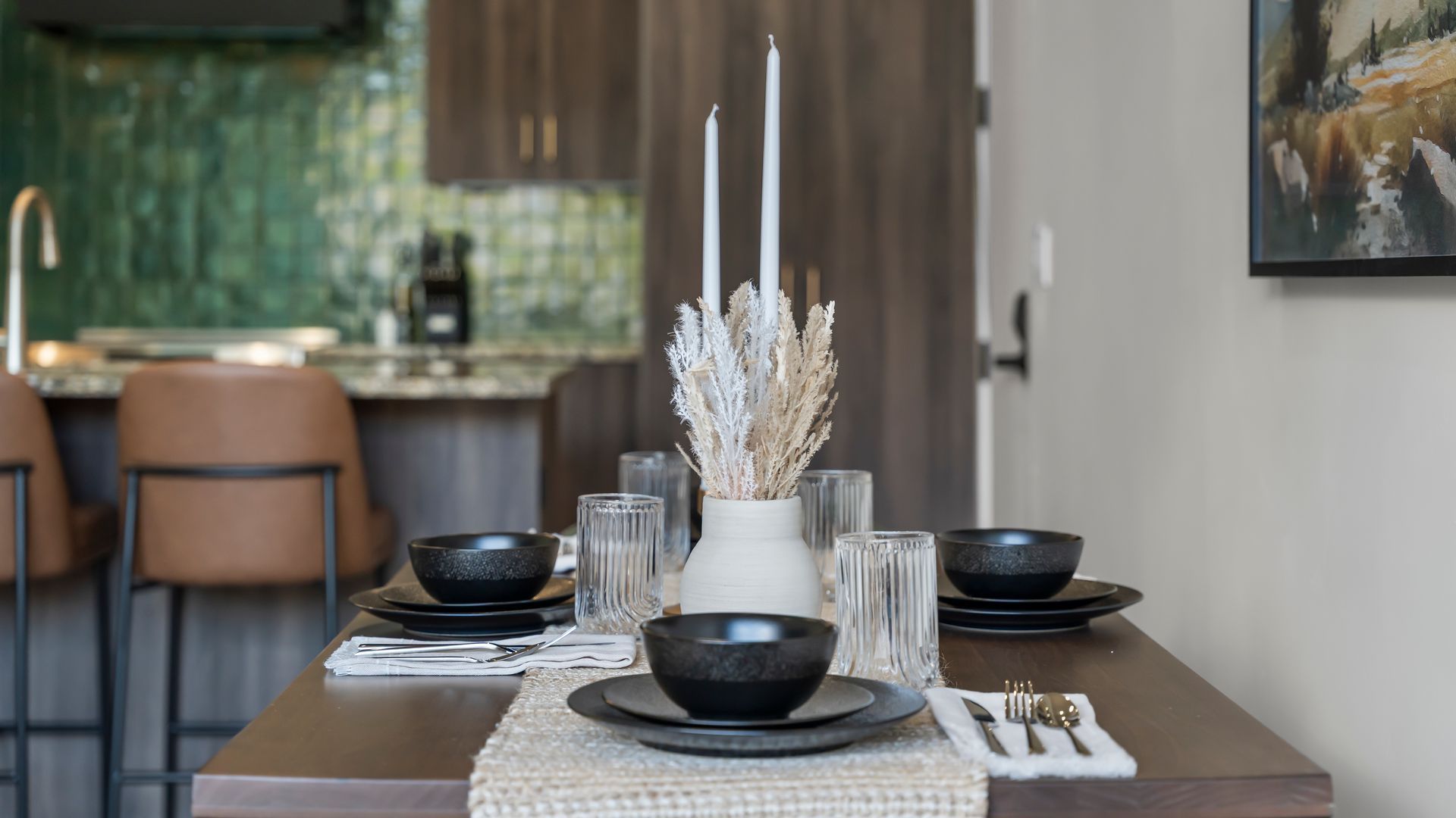 Dining table set for four with candles and bowls in front of a kitchen.