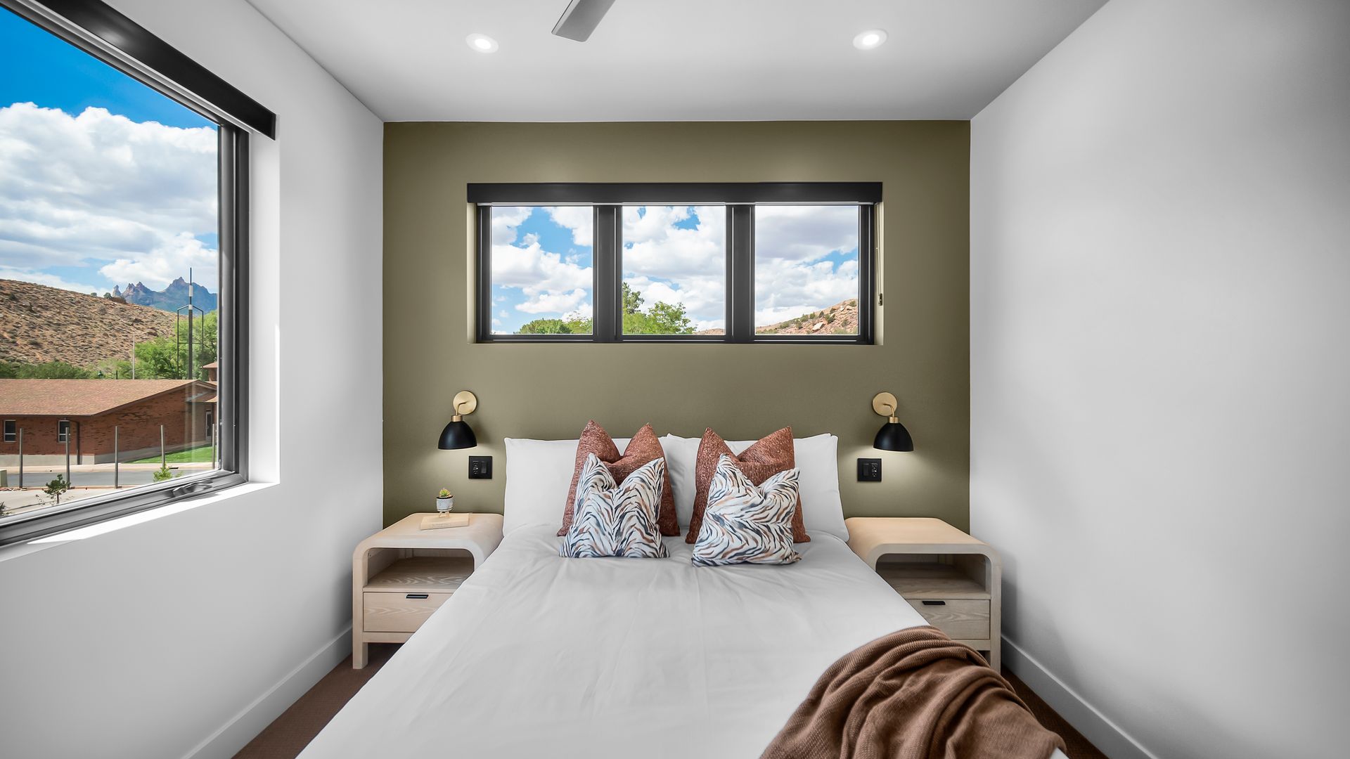 Bedroom with white walls, olive green accent wall, bed, nightstands, windows with scenic views.