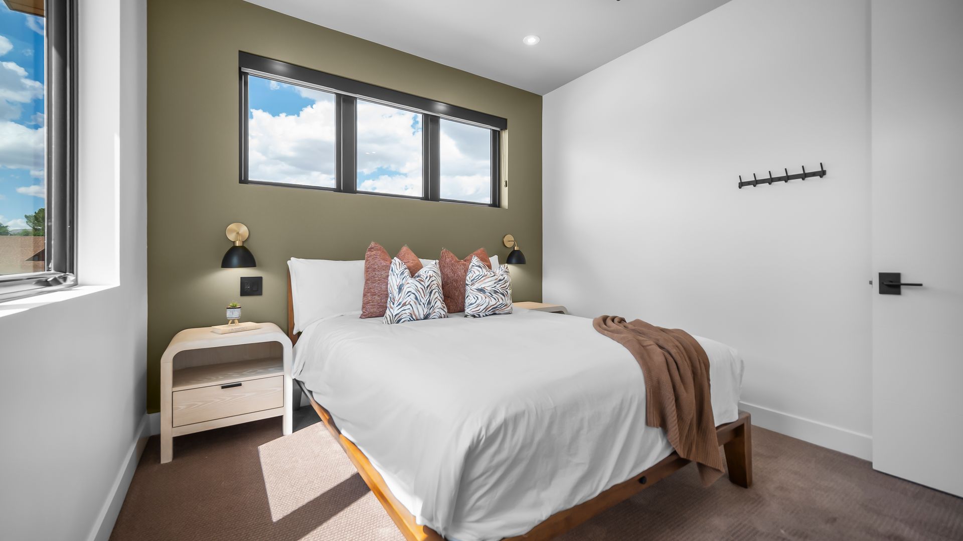 Bedroom with a white bed, olive green accent wall, and three windows.