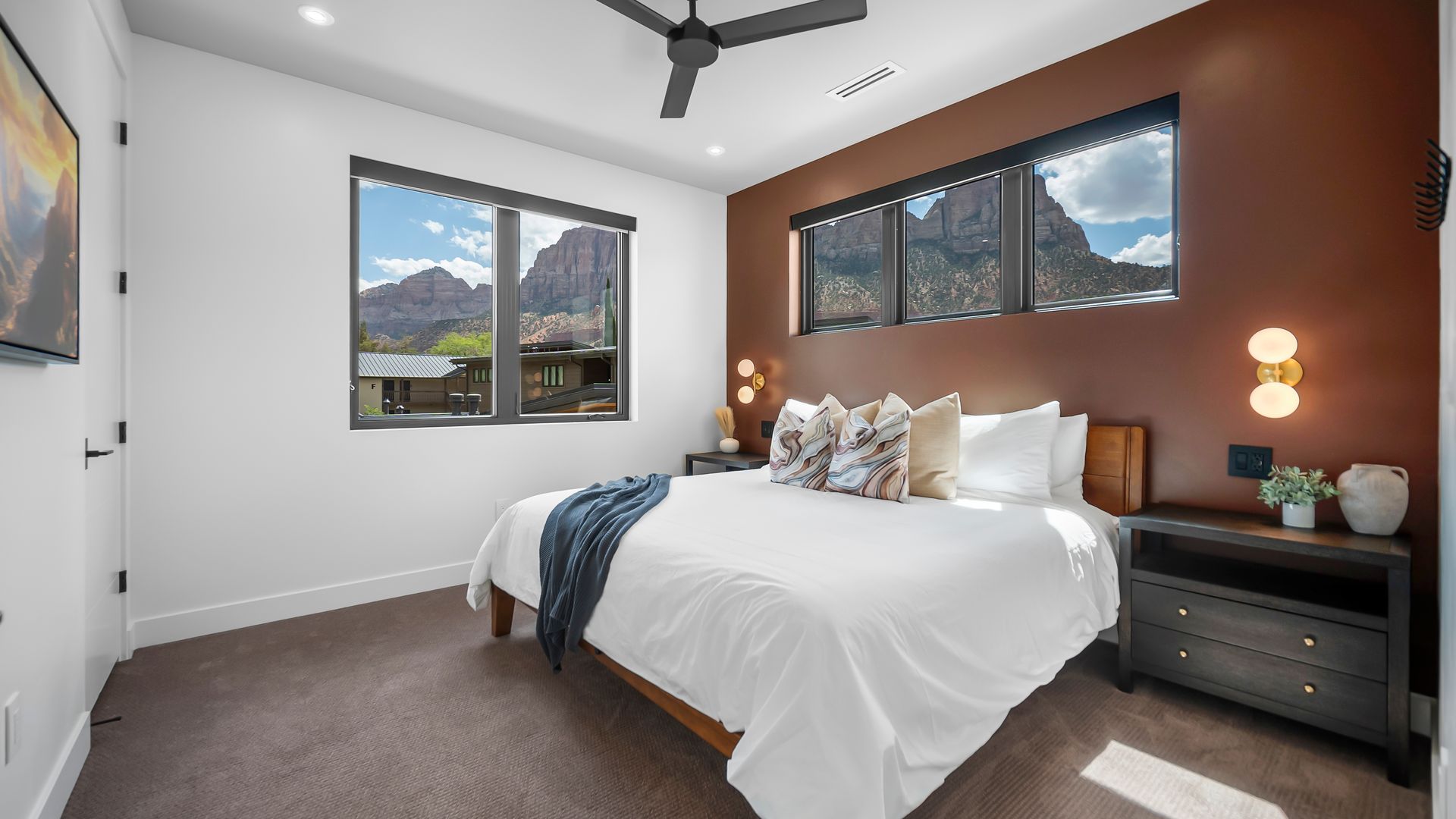 Bedroom with bed, dark brown accent wall, windows with mountain view.