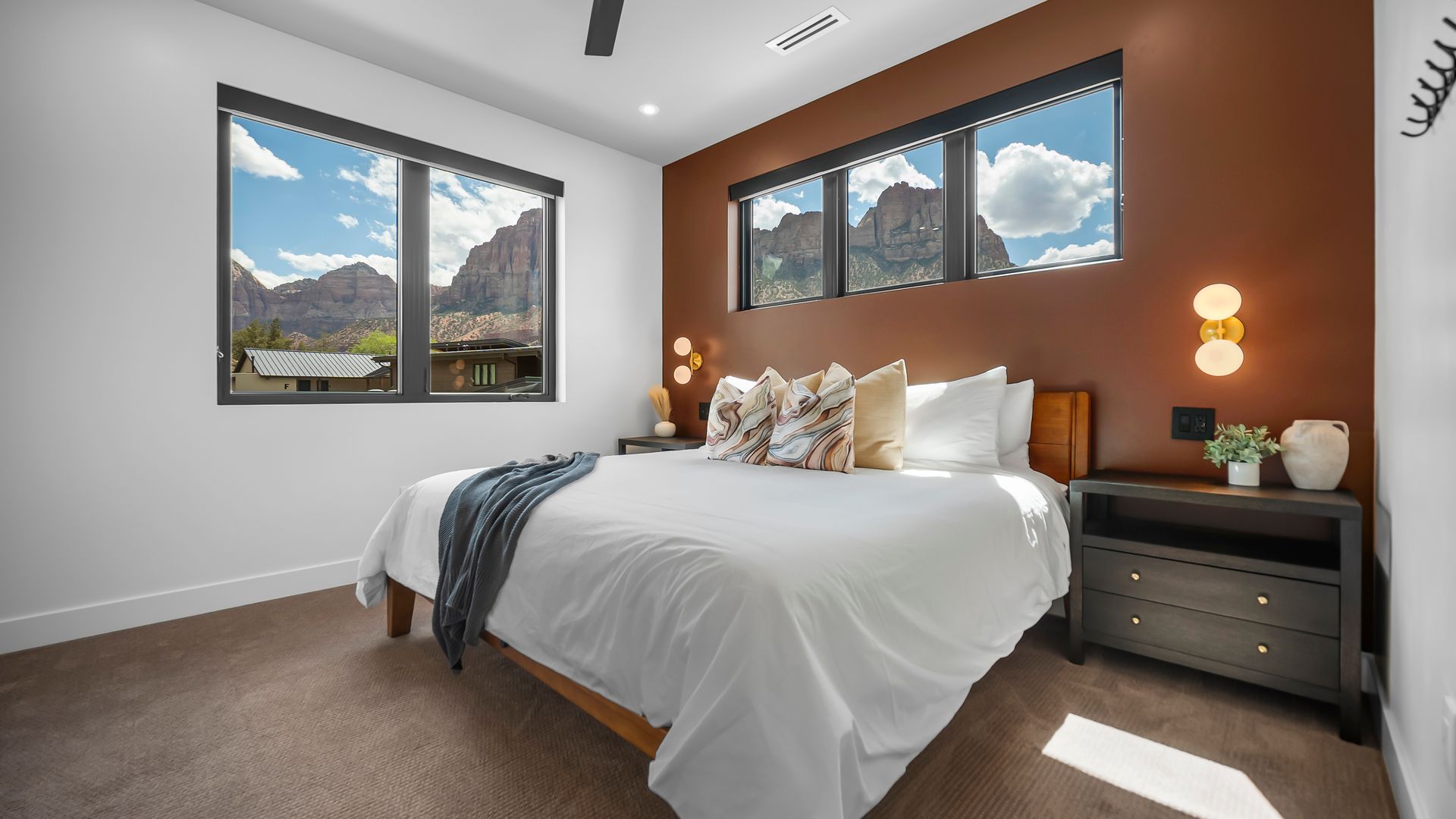 Bedroom with bed, windows looking out on mountains, brown accent wall, and dark furniture.