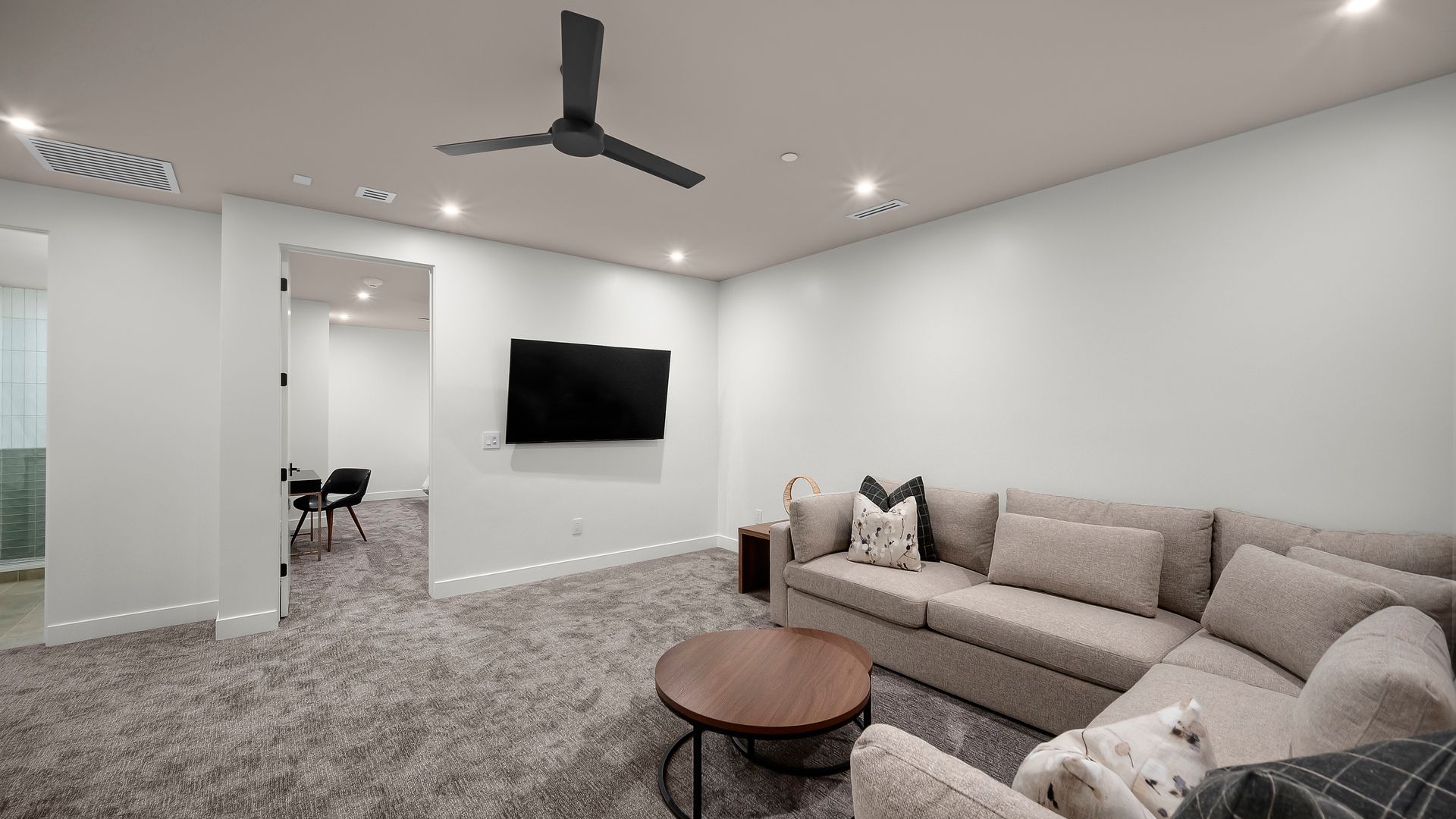 Living room with gray carpet, sectional sofa, round coffee table, and a mounted TV.