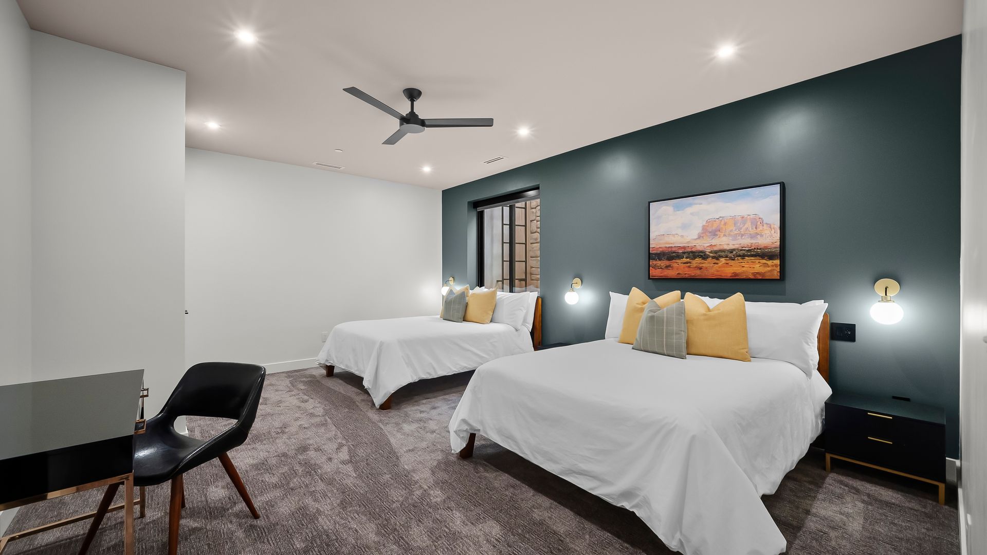 Bedroom with two beds, teal accent wall, artwork, desk, and gray carpet.