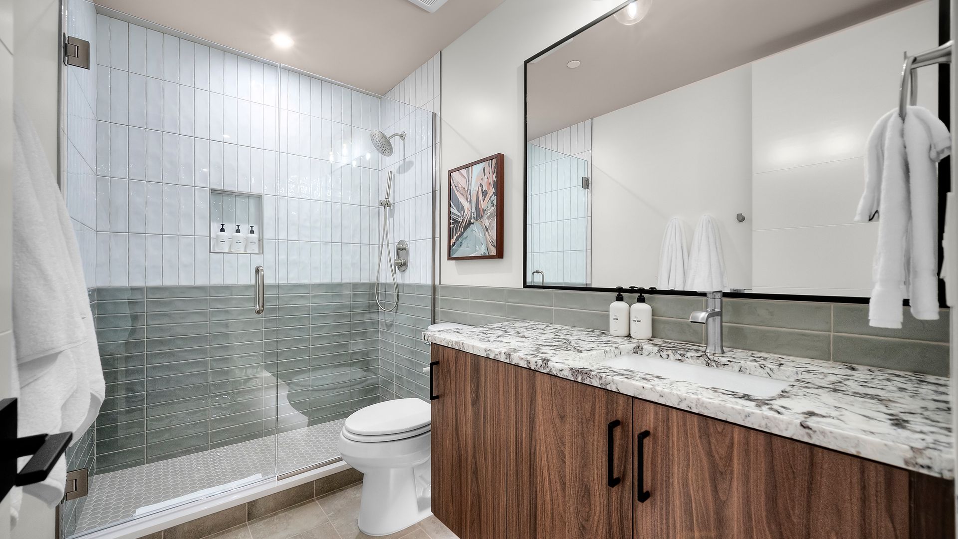 Modern bathroom with glass shower, wooden vanity, and white towels.