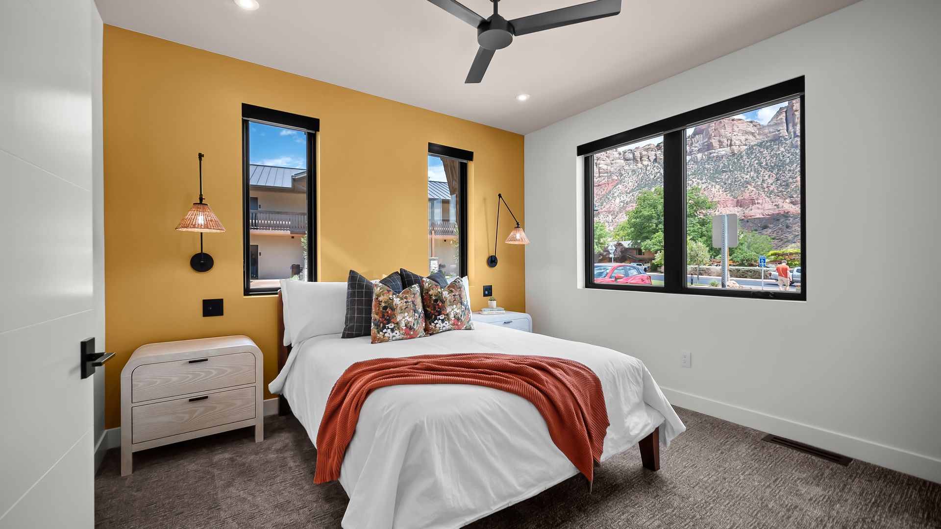 Bedroom with yellow accent wall, white bedding, black-framed windows, and decorative throw.