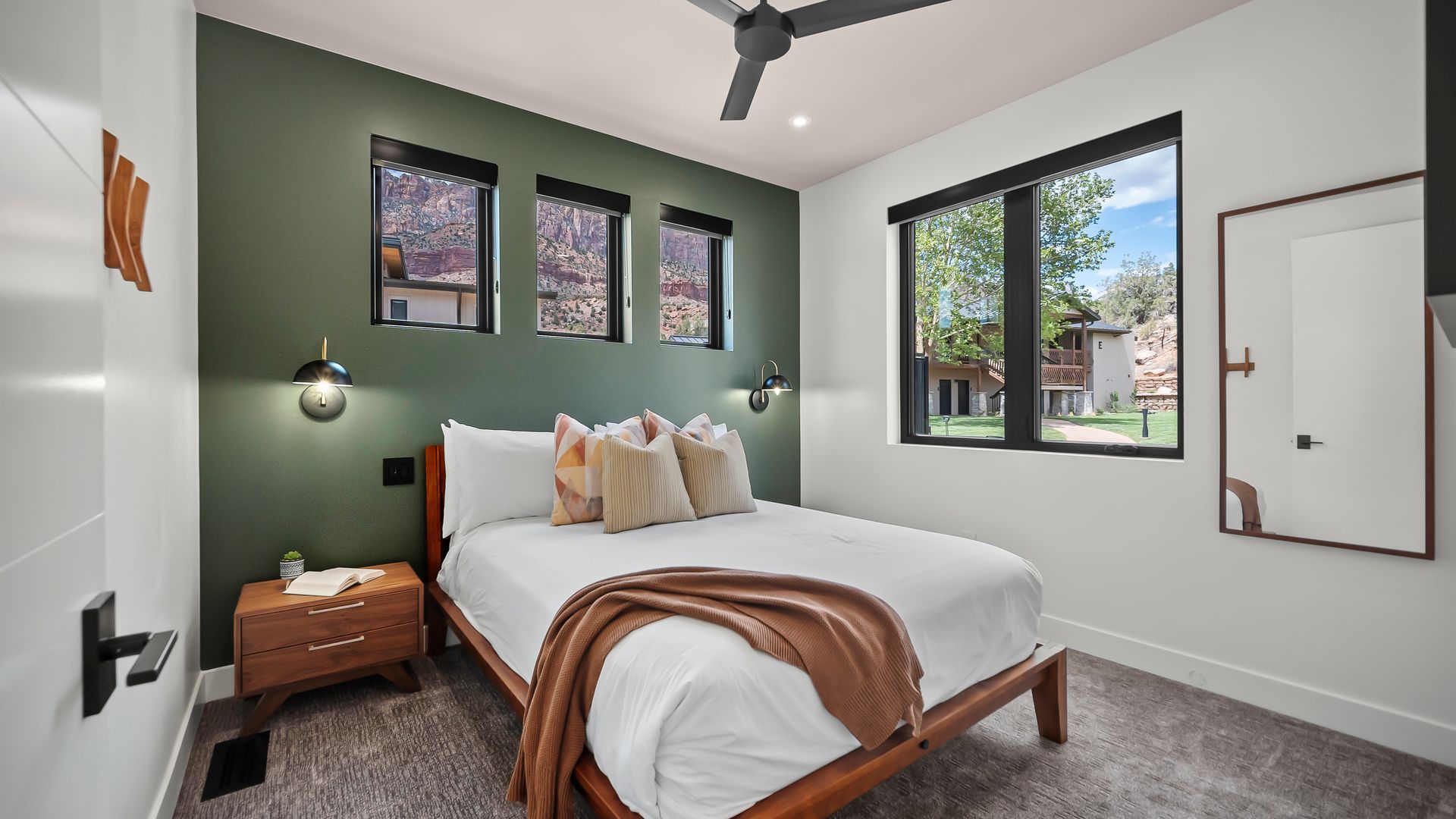 Bedroom with green accent wall, bed, nightstand, windows, and ceiling fan.