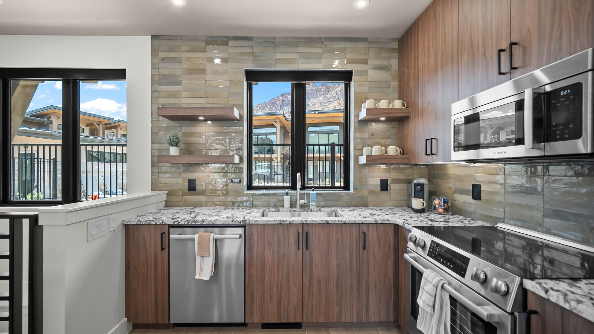 Modern kitchen with stainless steel appliances, wood cabinets, stone backsplash, and a window with a mountain view.
