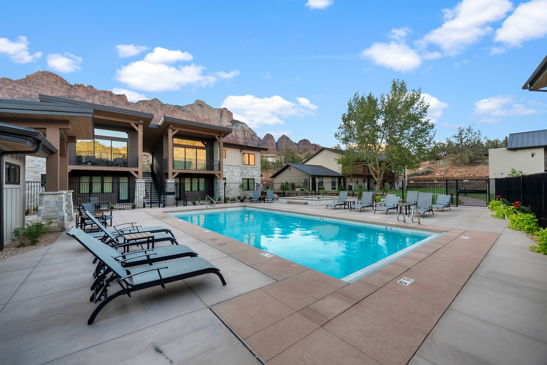 Swimming pool surrounded by lounge chairs, in front of a building with mountain backdrop.