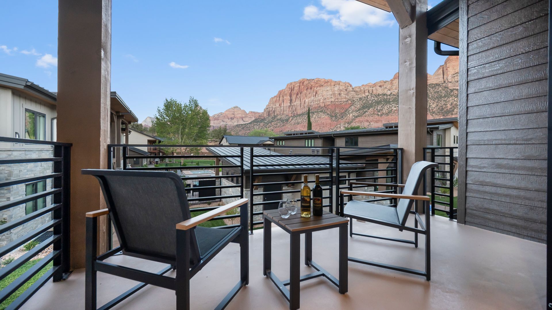 Balcony with two chairs, table, and wine overlooking red mountains.