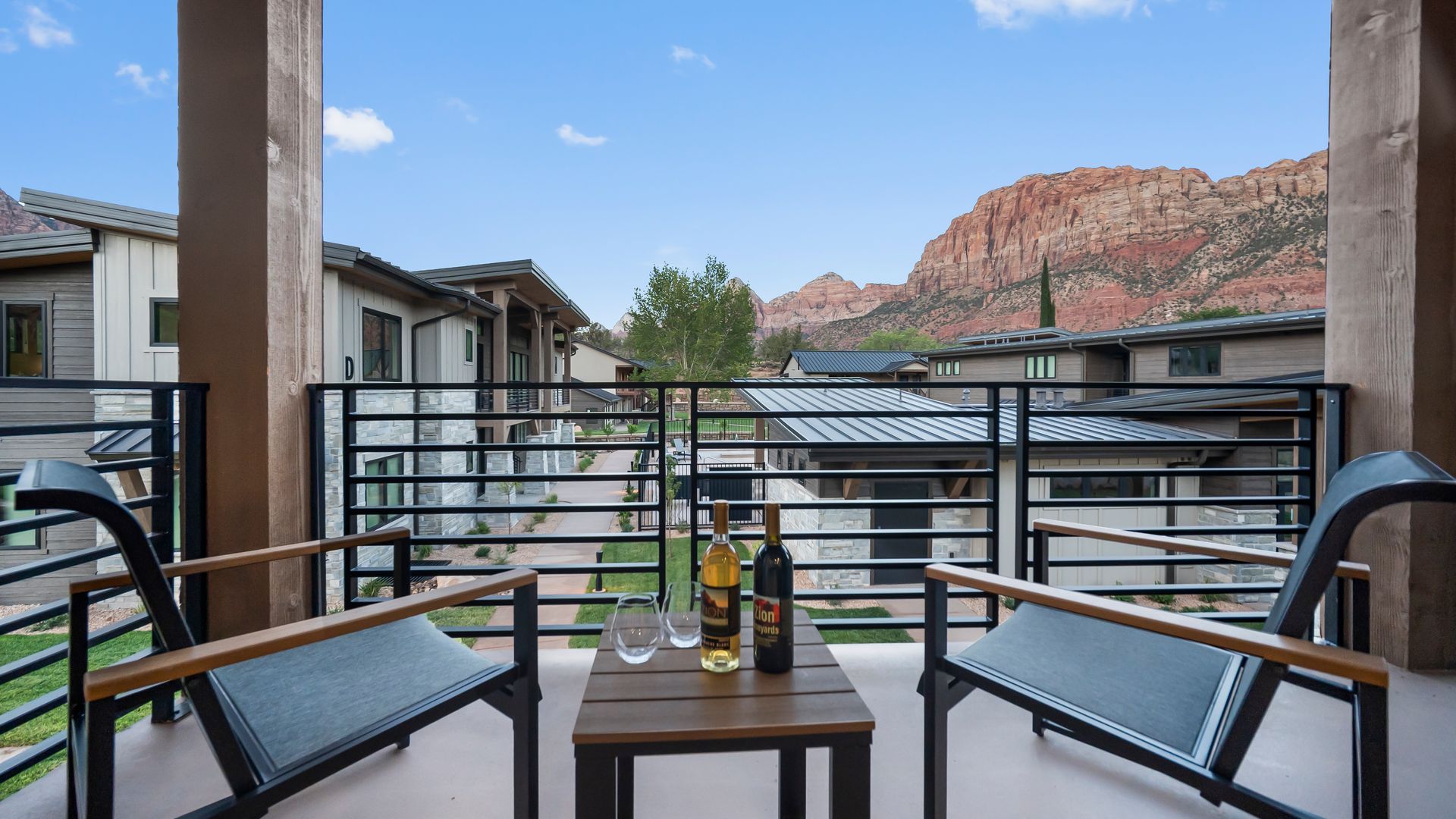 Balcony with two chairs, small table, wine bottles, and mountain view.