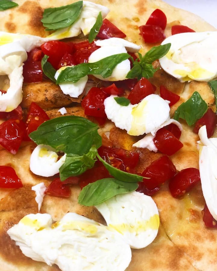 Focaccia condita con formaggio bianco, pomodorini e foglie di basilico fresco.