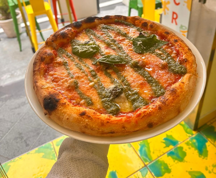 Pizza su un piatto bianco, condita con salsa verde, gialla e rossa in tre sezioni verticali.
