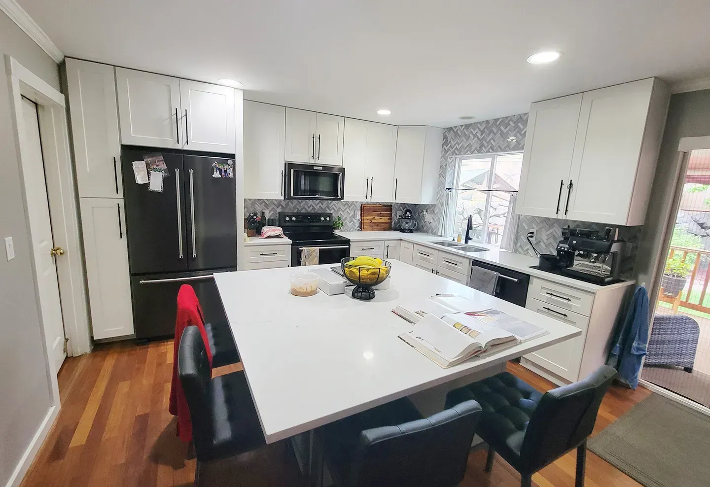 A kitchen with white cabinets , black appliances , a table and chairs.