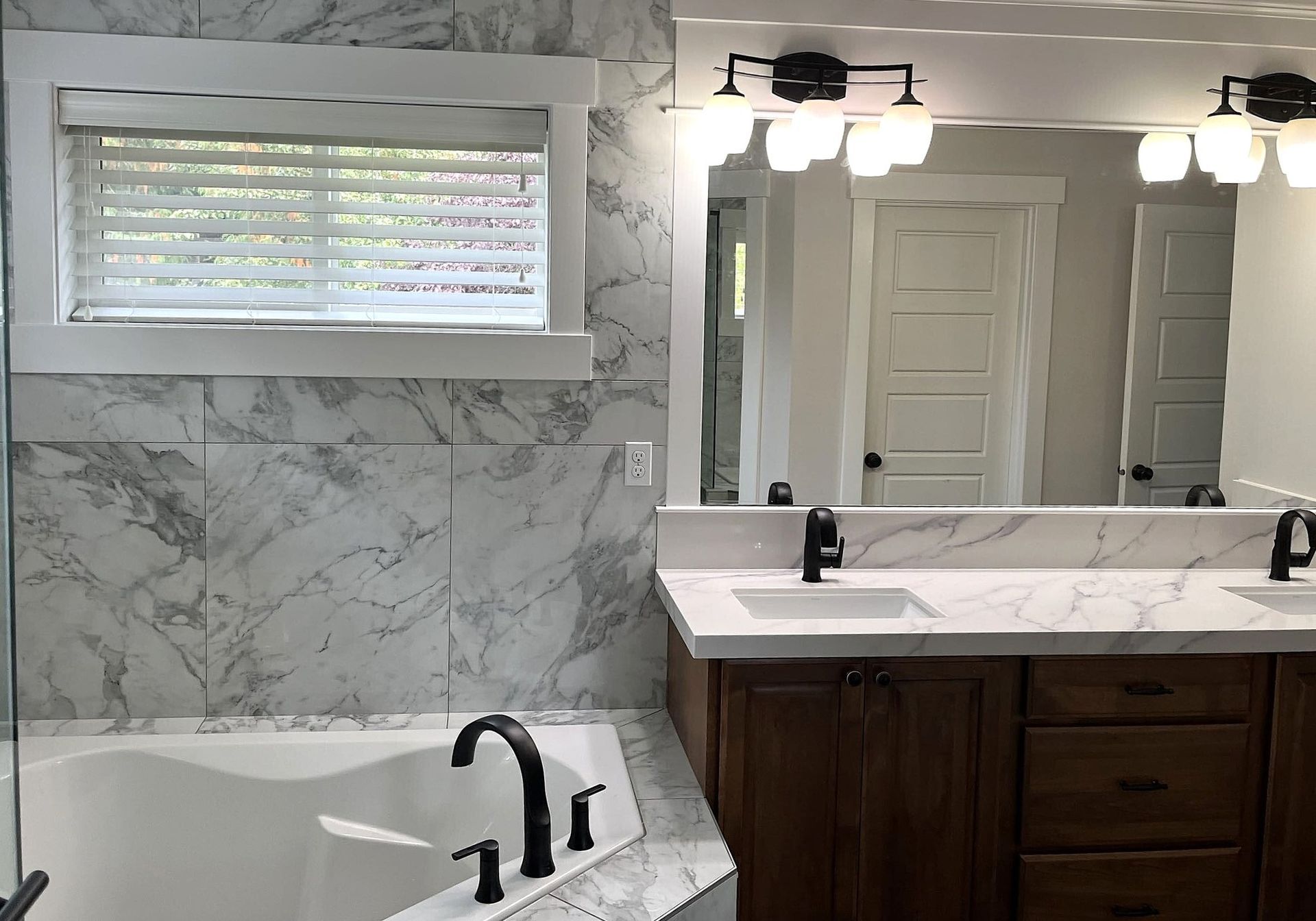 Bathroom with a tub, vanity, and marble-like tiled walls; natural light through window. Bathroom with a tub, vanity, and marble-like tiled walls; natural light through window.