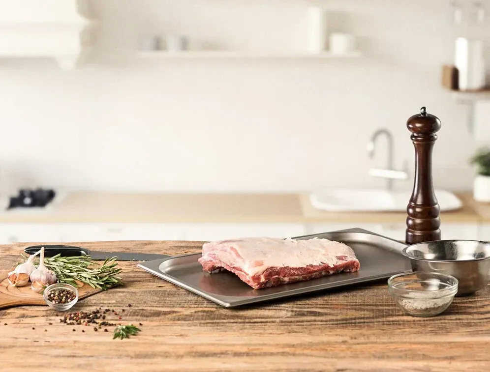 A piece of raw meat is sitting on a cutting board on a wooden table.