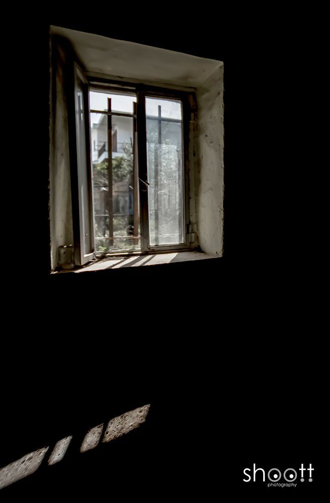 Zonlicht stroomt door een raam een ​​donkere, lege kamer binnen en werpt rechthoekige schaduwen op de vloer.