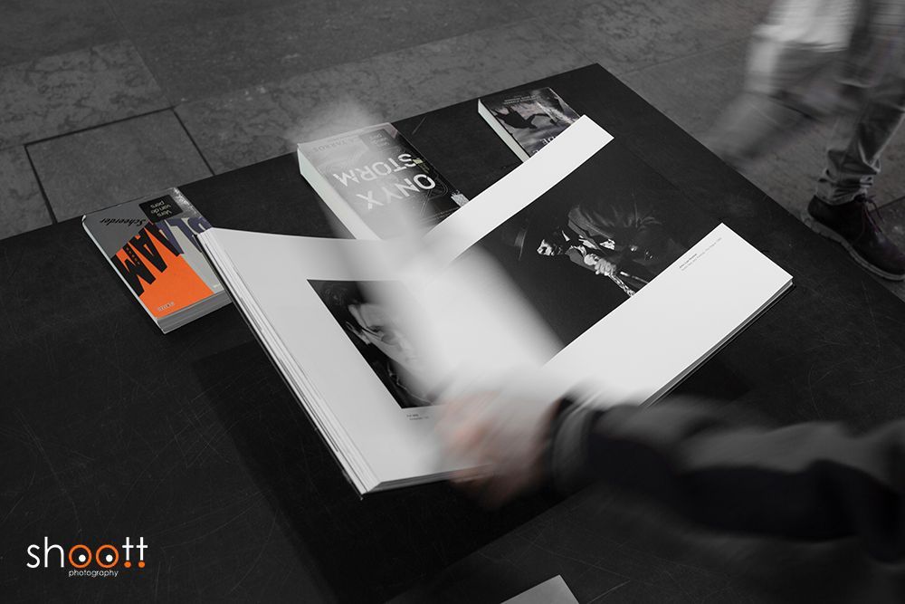 Door bewegingsonscherpte is te zien hoe een hand de bladzijden van een fotoboek omslaat op een zwarte achtergrond, met een tweede boek in de buurt.