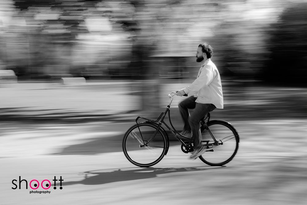 Een persoon fietst en profiel, vastgelegd met bewegingsonscherpte op de achtergrond om de snelheid te suggereren, in zwart-wit.