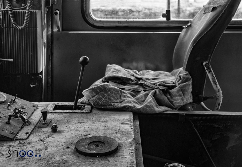 Een zwart-witfoto van een verweerde locomotiefcabine met een versnellingspook, versleten stoel en dashboard.
