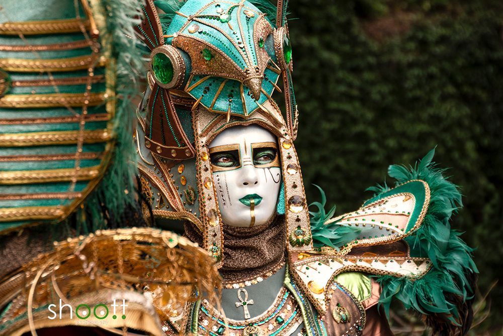 Persoon met een sierlijk Venetiaans masker en een uitgebreid turquoise en goudkleurig kostuum met een op de Egyptenaren geïnspireerde hoofdtooi.