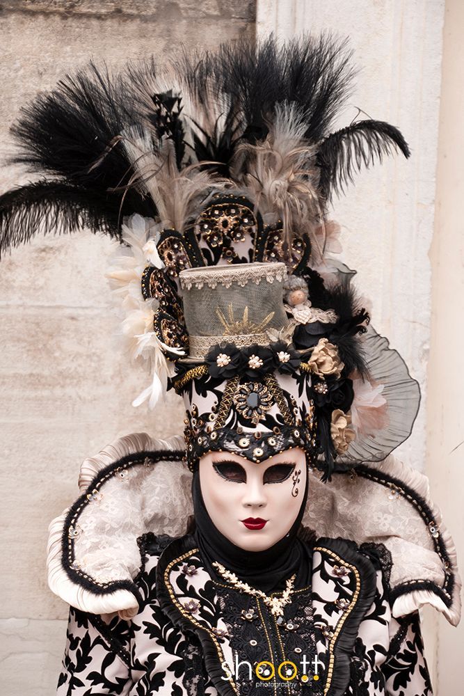 Een persoon in een zwart-wit Venetiaans carnavalskostuum, met een gedetailleerd masker en een sierlijke, met veren versierde hoge hoed.