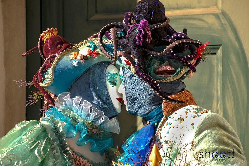 Twee personen in uitgebreide, op de zee geïnspireerde Venetiaanse kostuums en maskers kussen elkaar.