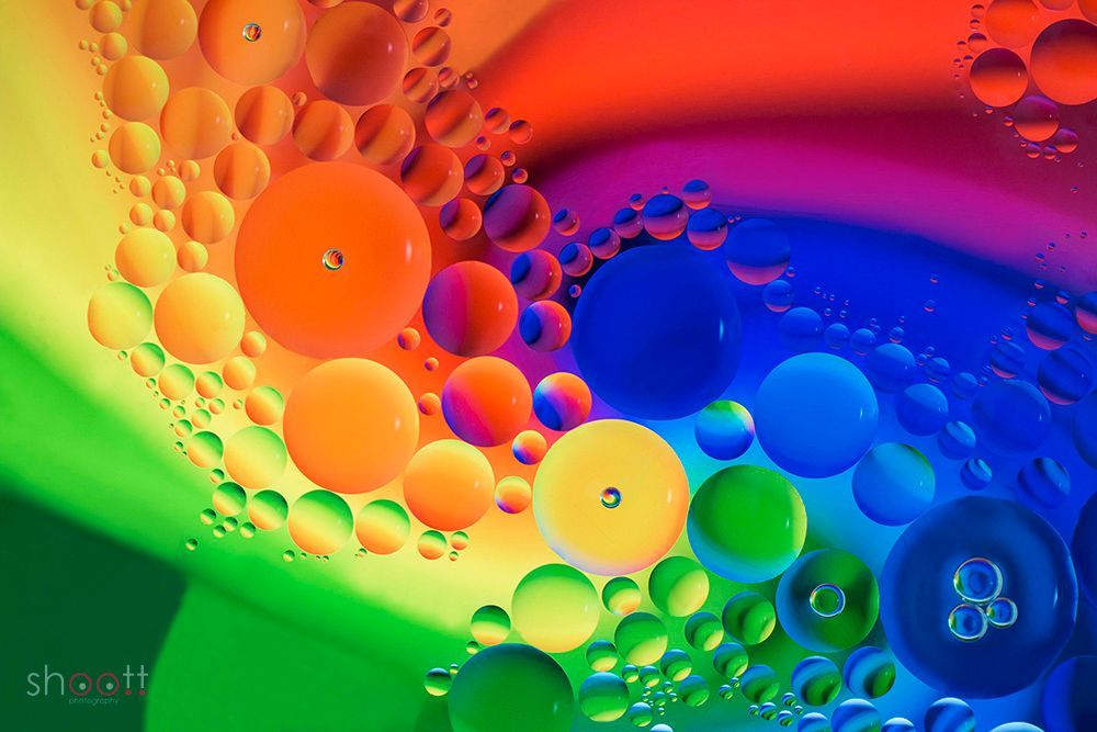 Abstracte macrofotografie van kleurrijke, glanzende oliedruppels die op water drijven en een levendig regenboogverloop creëren.